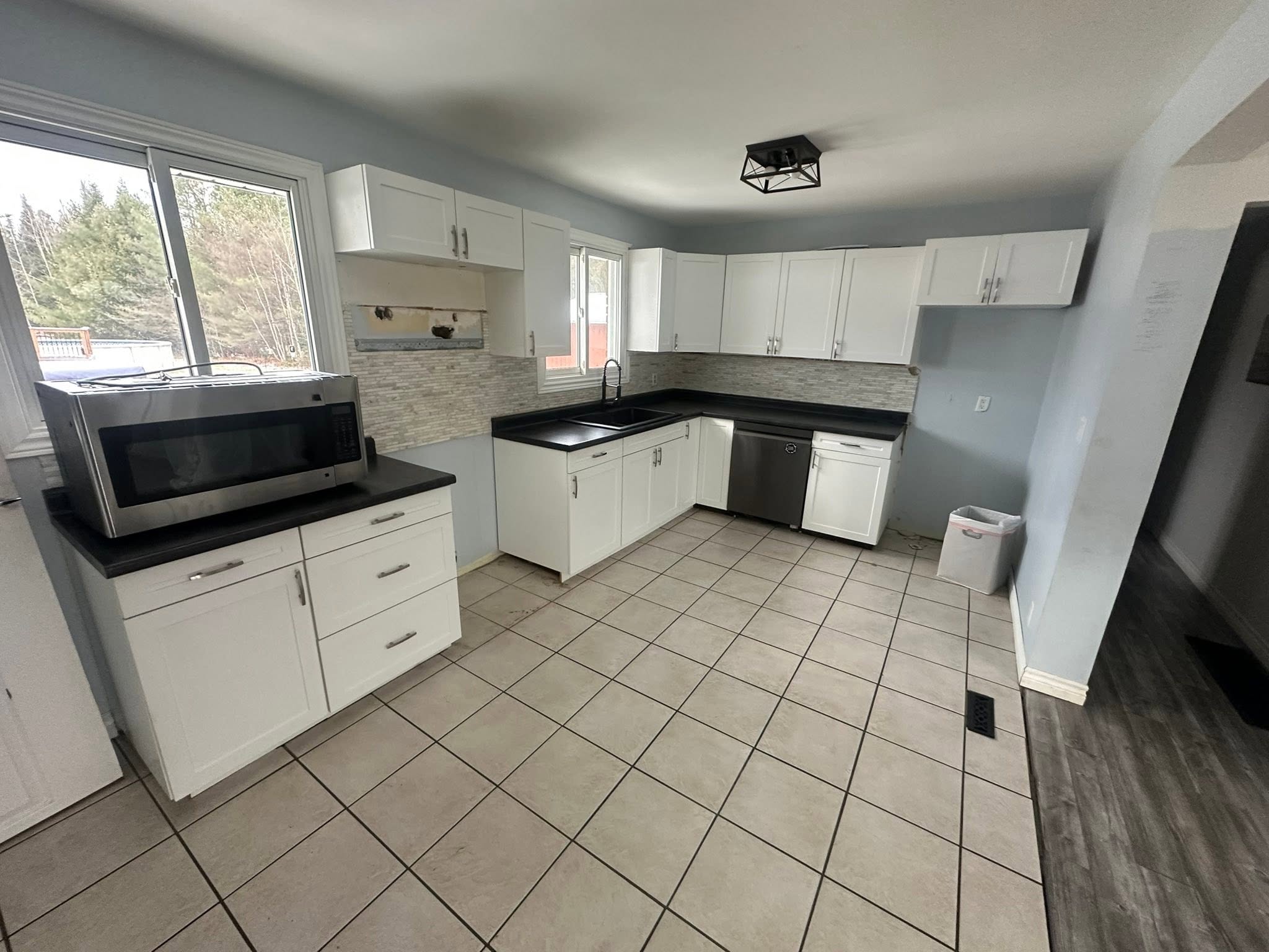 Kitchen before renovation, with white cabinets, black counters and a tiled floor